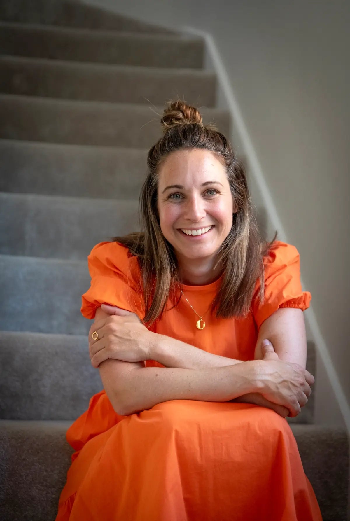 Lucy, the founder and lead interior designer of Homebird Studio, sat on the stairs, smiling and wearing an orange dress.